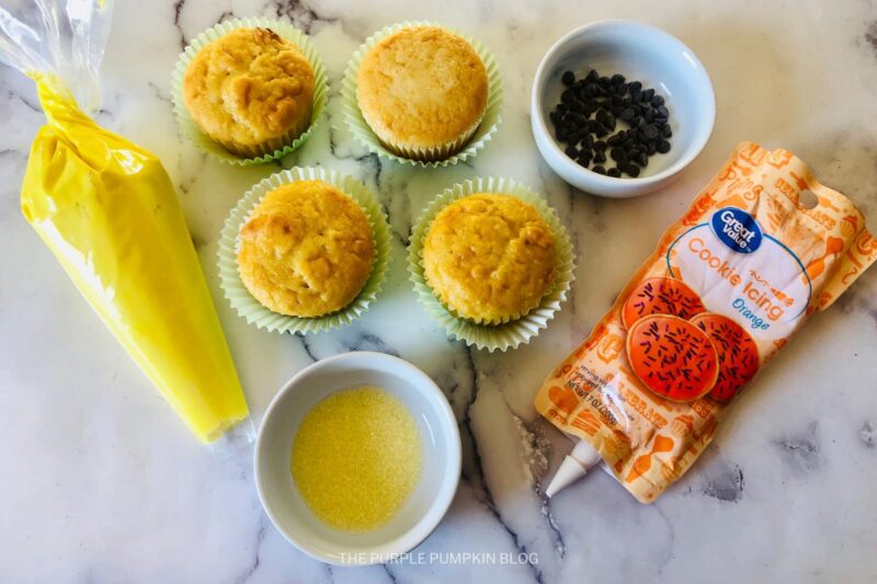 Ingredients for Baby Chick Cupcakes - cooked cupcakes, orange frosting, sanding sugar, chocolate chips and yellow frosting.
