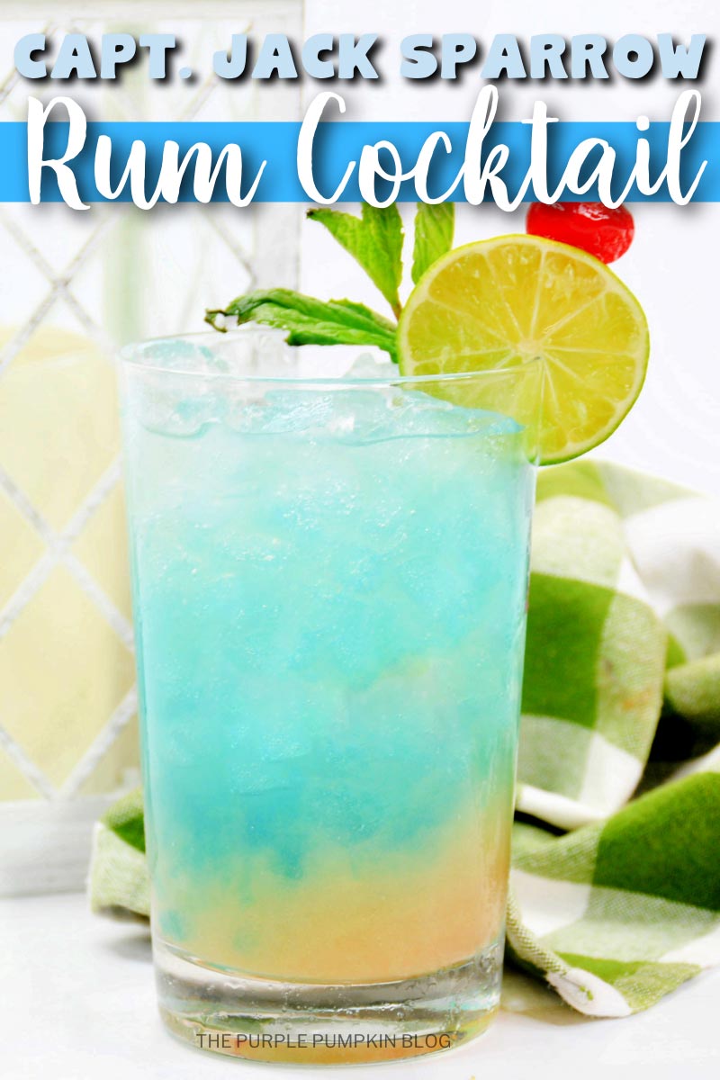 Glass of layered cocktail with yellow on the bottom and blue on the top, the glass is garnished with lime, mint and a cocktail cherry. A cloth and lantern are in the background. Text overlay says