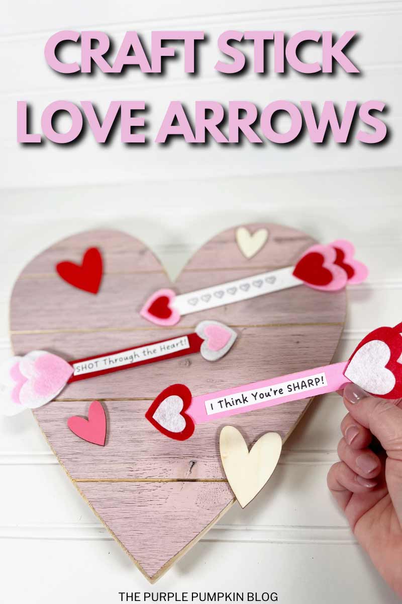 Love arrows made with wooden craft sticks laid on a large pink wooden heart platter. One arrow is held closer to the camera and in focus saying "I think you're sharp!". The other arrows have different sentiments on them. The text overlay says "Craft Stick Love Arrows". Similar craft images are featured throughout from various angles, and with different text overlays, unless otherwise described.