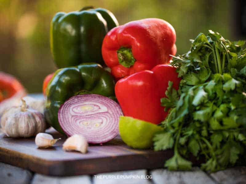 bell peppers, red onion, limes, garlic, and cilantro on a chopping board.
