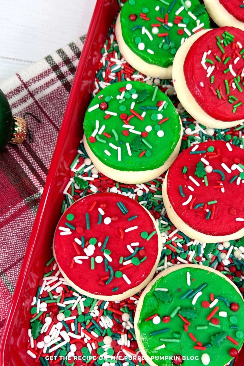 A red platter covered in red, white, and green sprinkles, and topped with homemade Lofthouse-style cookies, frosted with either red or green frosting and covered with more sprinkles.