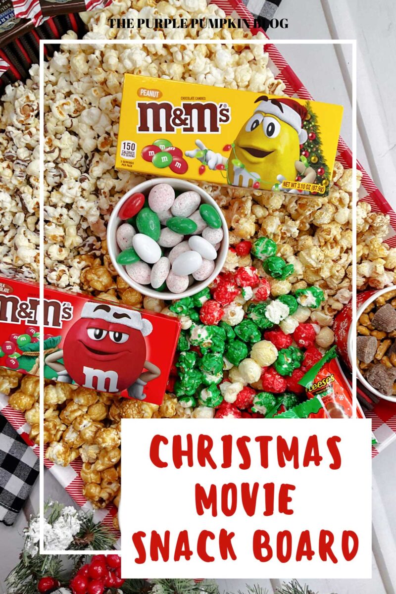 A red gingham tray, filled with pots of candy, pretzels, and chocolate chips, surrounded by various popcorn flavors, and topped with boxes of M&Ms and packets of Reese's Christmas Trees.