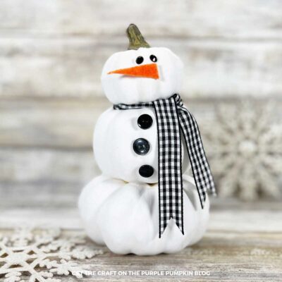 A stack of plastic pumpkins, painted white and decorated with black buttons, rhinestones, ribbon, and felt to look like a snowman.
