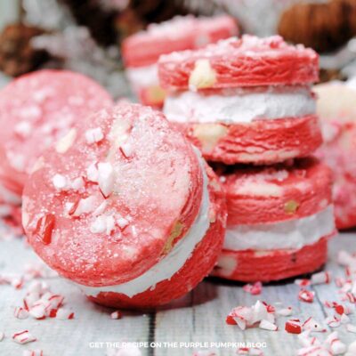 A pile of red velvet cookies, sandwiched with vanilla frosting and decorated with crushed candy canes.