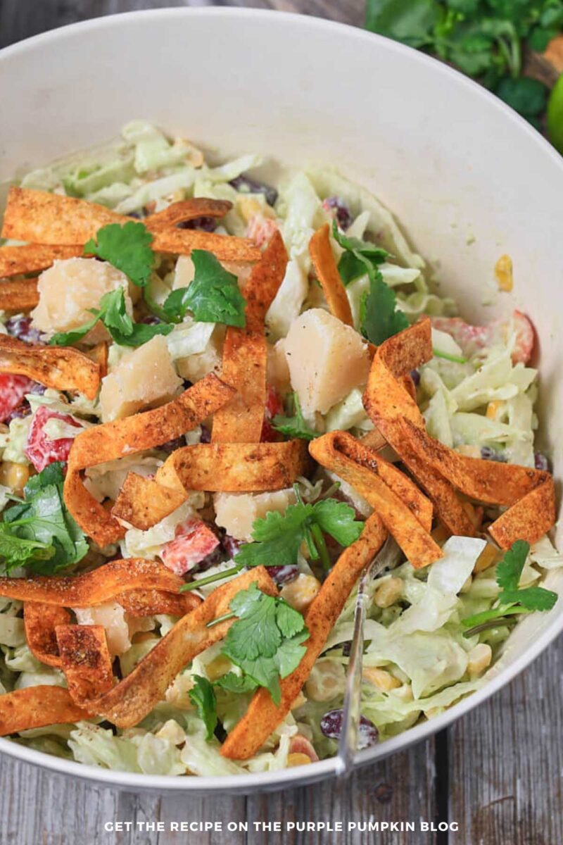 Bowl of salad - beans, corn, lettuce, bell peppers - tossed with avocado dressing and garnished with cheese and crispy tortilla strips.