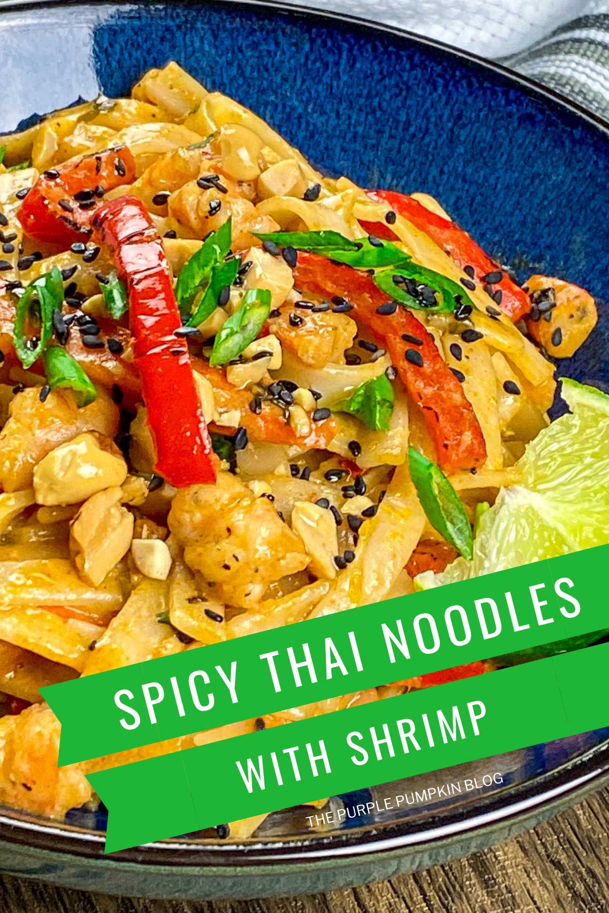 Bowl of noodles, shrimp and veggies in a creamy sauce, garnished with peanuts, sesame seeds and lime wedges. Text overlay says: Spicy Thai Noodles with Shrimp