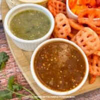 Bowls of red and green taco sauce with other taco toppings in the background.