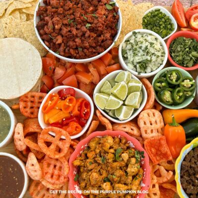 A wooden board covered with bowls of taco meat, sauces, and toppings for street tacos.