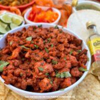 A bowl filled with tacos al pastor, garnished with chopped herbs and surrounded by taco fixins.