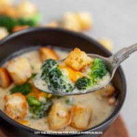 Bowl of broccoli soup garnished with additional broccoli, croutons with a spoonful of soup in the foreground focus.