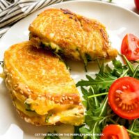 Grilled cheese on a white plate next to a stripe cloth, and additional ingredients scattered around.