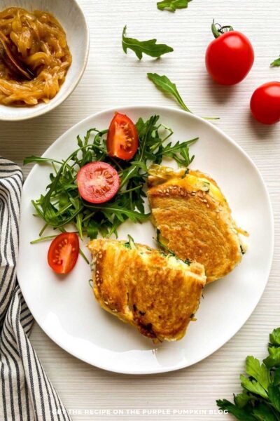 Grilled cheese on a white plate next to a stripe cloth, and additional ingredients scattered around.