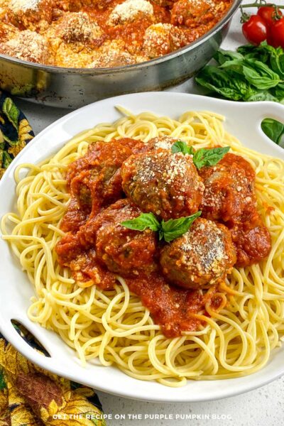 A bowl of spaghetti with meatballs. With a pan of meatballs in the background.