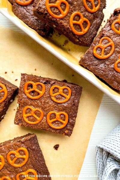 Squares of Pretzel Chocolate Brownies on some parchment paper, with pretzels scattered around.