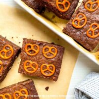 Squares of Pretzel Chocolate Brownies on some parchment paper, with a tray of more brownies to the side.