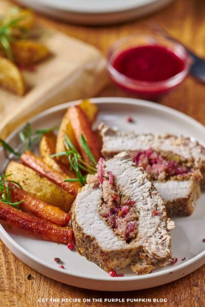 Slices of stuffed pork tenderloin with roasted carrots and potatoes on a white plate