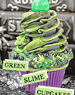 Cupcake topped with frosting and green and black sprinkles, with another swirl of black and green frosting on top with a green candy ball to finish. Halloween decor is in the background. Text overlay says: Halloween Green Slime Cupcakes