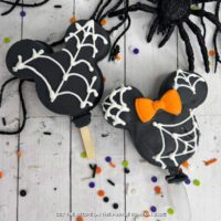 Mickey Mouse-shaped Oreo Cookie Pops, covered with black candy melts and white candy spiderwebs. Minnie has an orange bow.with Halloween decorations scattered around.
