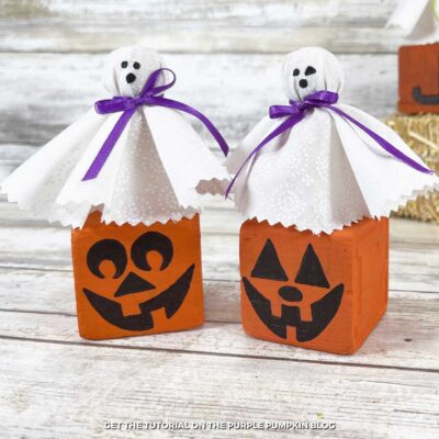 Orange-painted wooden cubes with Jack-o'-Lantern faces draw on. Fabric ghosts sit on top of the cubes.