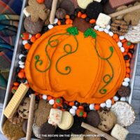 A tray with an orange-frosting pumpkin in the center surrounded by a selection of cookie dippers. Fall decor surrounds the tray.