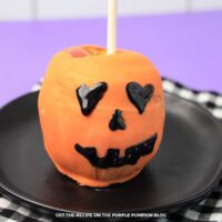 An apple dipped in orange candy melts and decorated with black icing to create a Jack-o'-Lantern face.