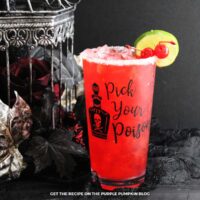 Red drink inside a glass that is embossed with a poison bottle and the words "Pick Your Poison". Glass is garnished with salt rim, red maraschino cherries and a slice of lime. Halloween decor is in the background.