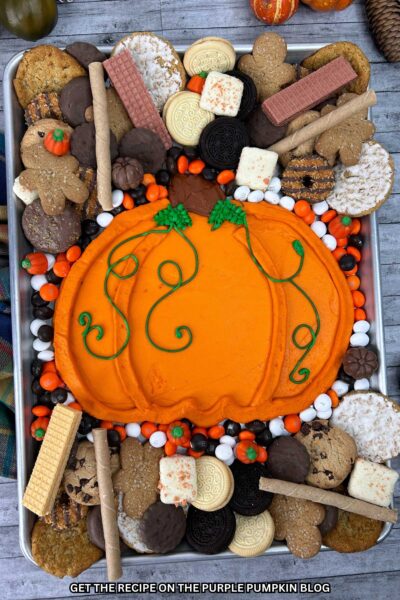 A tray with an orange-frosting pumpkin in the center surrounded by a selection of cookie dippers. Fall decor surrounds the tray.