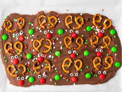 Thin piece of chocolate covered with mini pretzels, red and green candies, candy eyes and festive sprinkles.