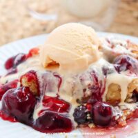 A plate with a portion of cherry dump cake topped with additional cherries and a scoop of ice cream.