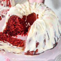 A red velvet bundt cake covered with frosting and pink sprinkles, with slices cut out and served on a plate.