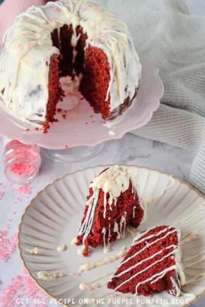A red velvet bundt cake covered with frosting and pink sprinkles, with slices cut out and served on a plate.