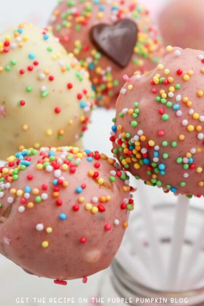 A selection of round and heart-shaped cake pops covered with white, pink, and red chocolate and sprinkles.