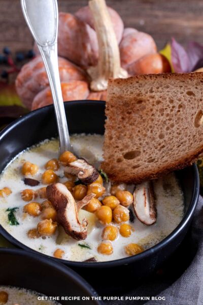 Bowls filled with mushroom spinach soup, garnished with slices of mushroom, chickpeas and toasted bread.