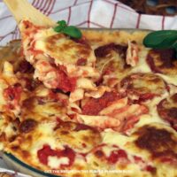 Close up of pepperoni pizza mac n cheese in a baking dish with a serving being scooped out and text overlay: Pepperoni Pizza Mac n Cheese Recipe