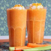 Glasses filled with orange, carrot cake smoothies and topped with coconut whipped cream, chopped nuts, and orange zest.