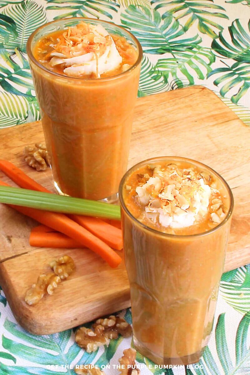 Glasses filled with orange, carrot cake smoothies and topped with coconut whipped cream, chopped nuts, and orange zest.