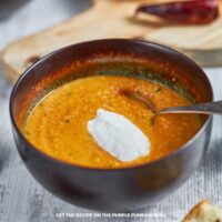Bowl of carrot and lentil soup topped with a dollop of sour cream. Some ingredients are scattered around the bowl.