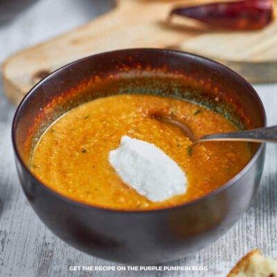 Bowl of carrot and lentil soup topped with a dollop of sour cream. Some ingredients are scattered around the bowl.