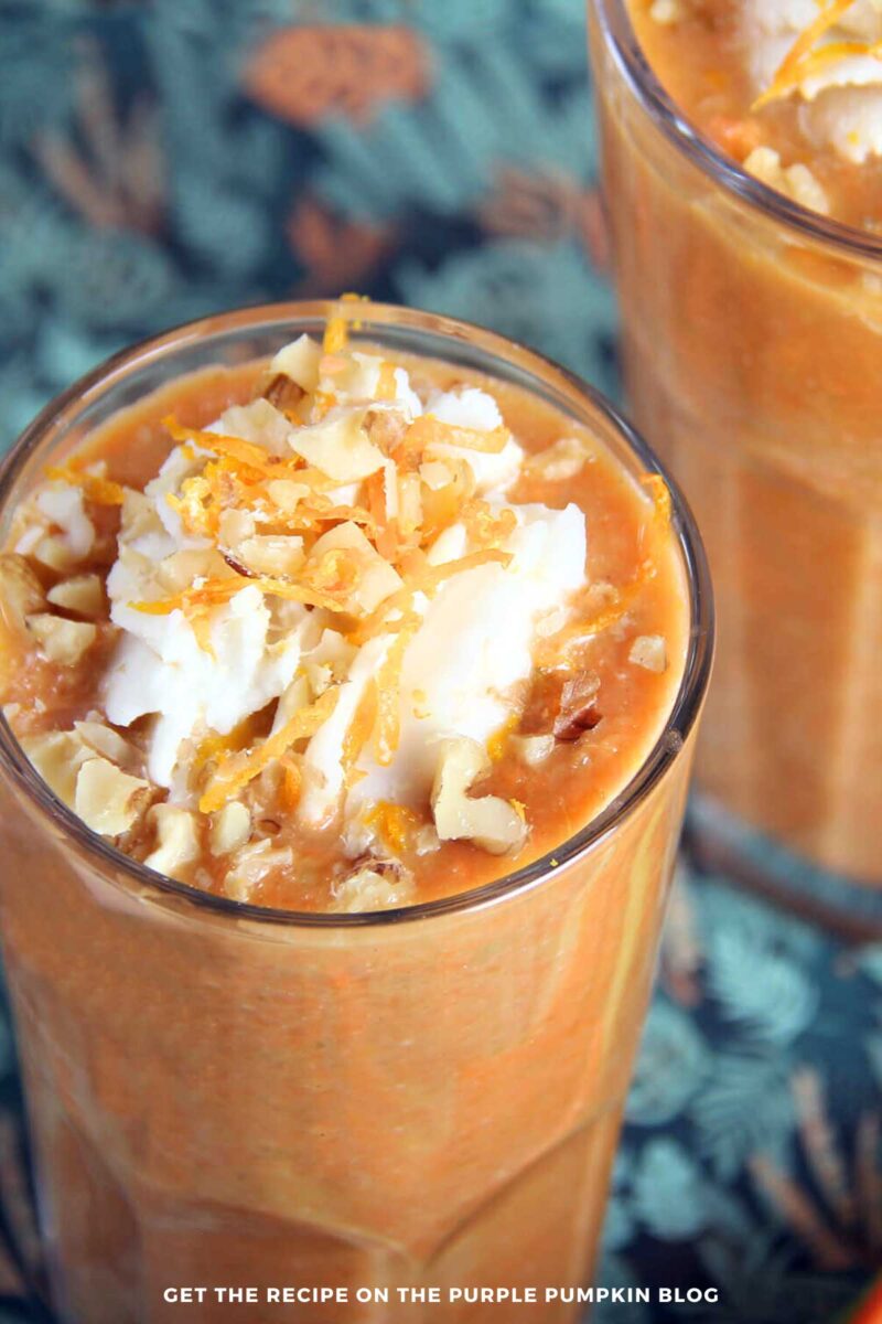 Glasses filled with orange, carrot cake smoothies and topped with coconut whipped cream, chopped nuts, and orange zest.
