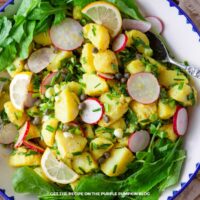 A bowl filled with potato salad made with capers, sliced radish, and lemon-oil dressing, garnished with chopped chives.