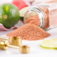 Homemade Tajin Spice Blend tipped out of a jar onto a work surface surrounded by limes.