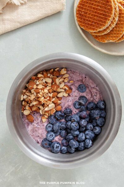 Fresh blueberries and chopped almonds added to the blended ice cream mixture in a mixing bowl.