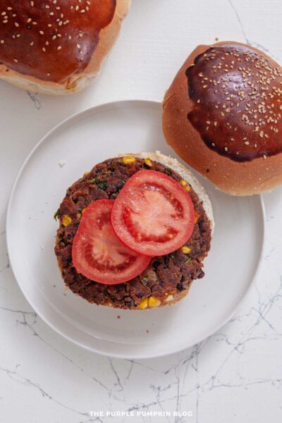 A white plate topped with a black bean burger and a tomato in a bun