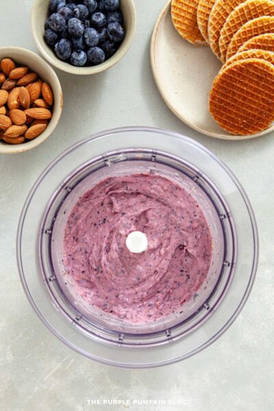 Blueberry ice cream mixture blended smooth inside a food processor bowl.
