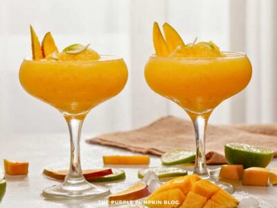 Two glasses of mango coconut daiquiri garnished with mango slices and lime zest