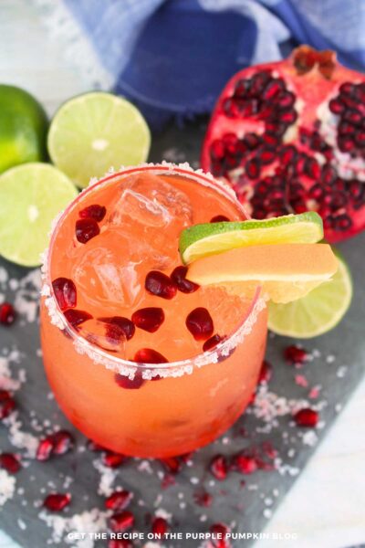 Festive pomegranate orange margarita in a glass with salted rim, lime, orange, and pomegranate garnish