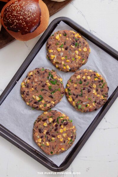 Four uncooked veggie burger patties shaped and placed on a parchment-lined baking tray