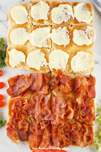 The bottom halves of the slider buns layered with crispy bacon on top of the tomato slices, with mayo-coated tops nearby.