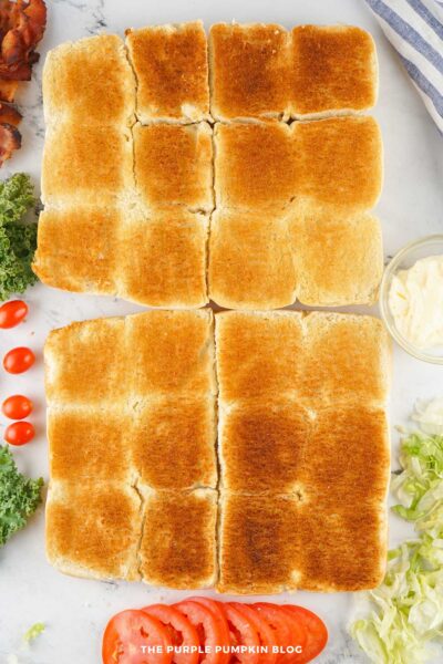 The tops and bottoms of the slider buns after toasting, golden brown and ready for assembly, with surrounding ingredients.