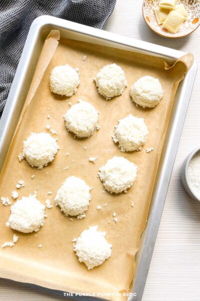 Neatly scooped unbaked coconut macaroons arranged on a parchment-lined baking tray, ready for the oven.
